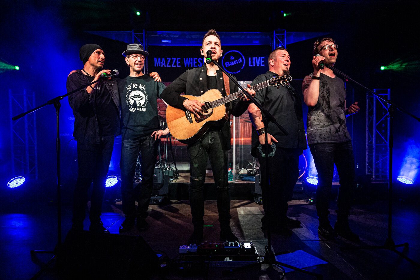 Die Band gemeinsam an den Mikrofonen, mehrstimmiger Gesang im Konzert